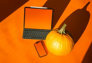 Pumpkin next to a laptop and a mobile phone sitting on an orange tabletop